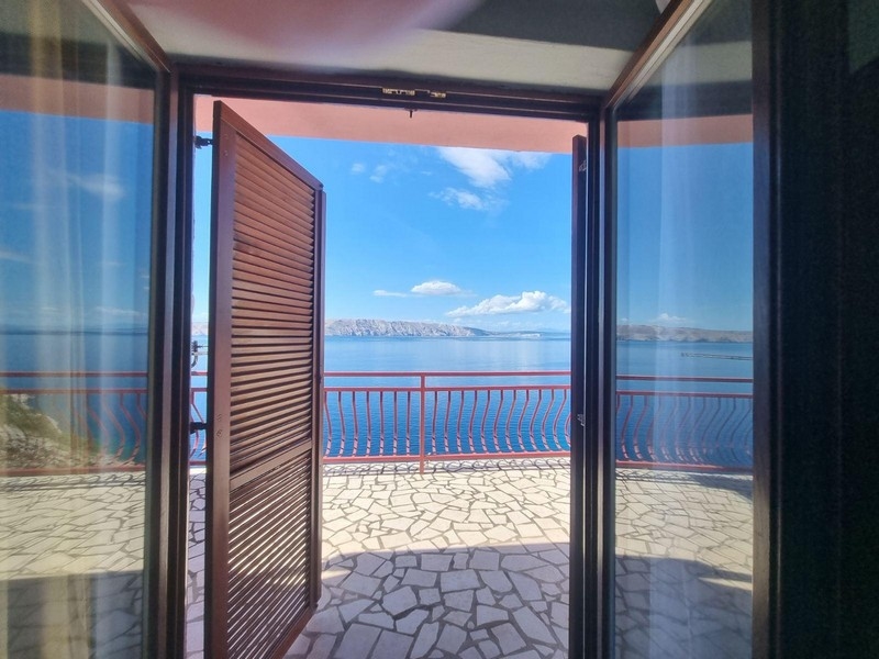 Widok z pokoju przez otwarte drzwi na taras z widokiem na morze.