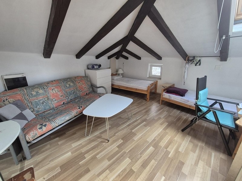 Otwarta przestrzeń mieszkalna na poddaszu z dwoma łóżkami i drewnianymi belkami na suficie.