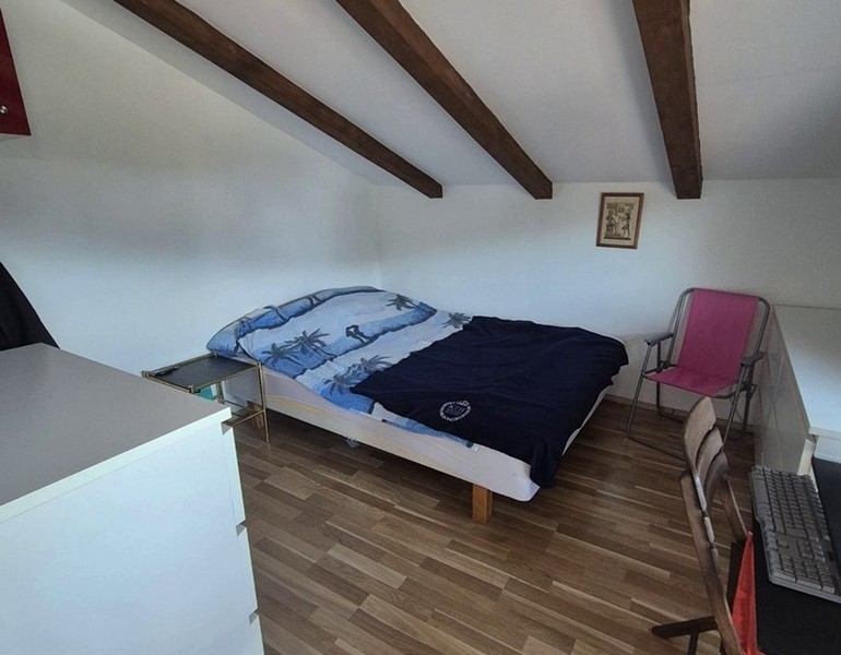 Sypialnia na poddaszu z drewnianymi belkami i podwójnym łóżkiem.