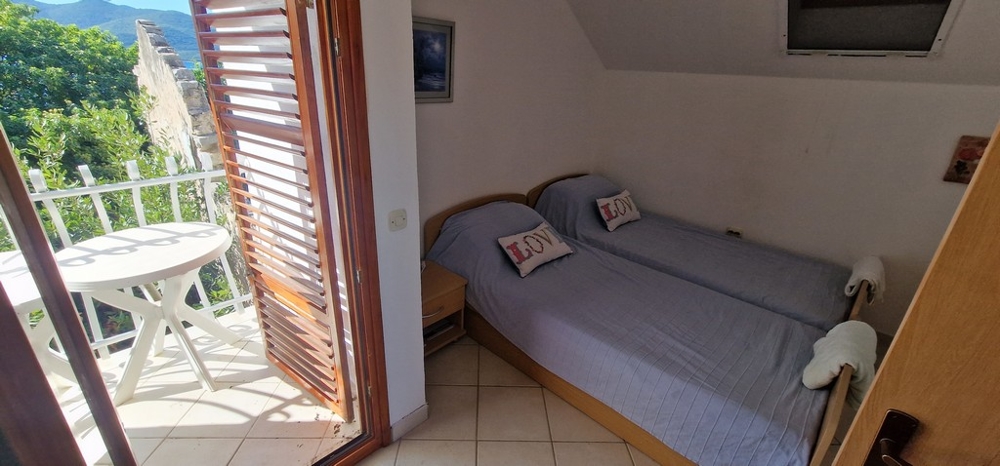 Sypialnia z dwoma pojedynczymi łóżkami przykryta niebieskimi kocami. Do dyspozycji Gości jest niewielki balkon z okrągłym stołem i krzesłami oraz widok na zieleń.