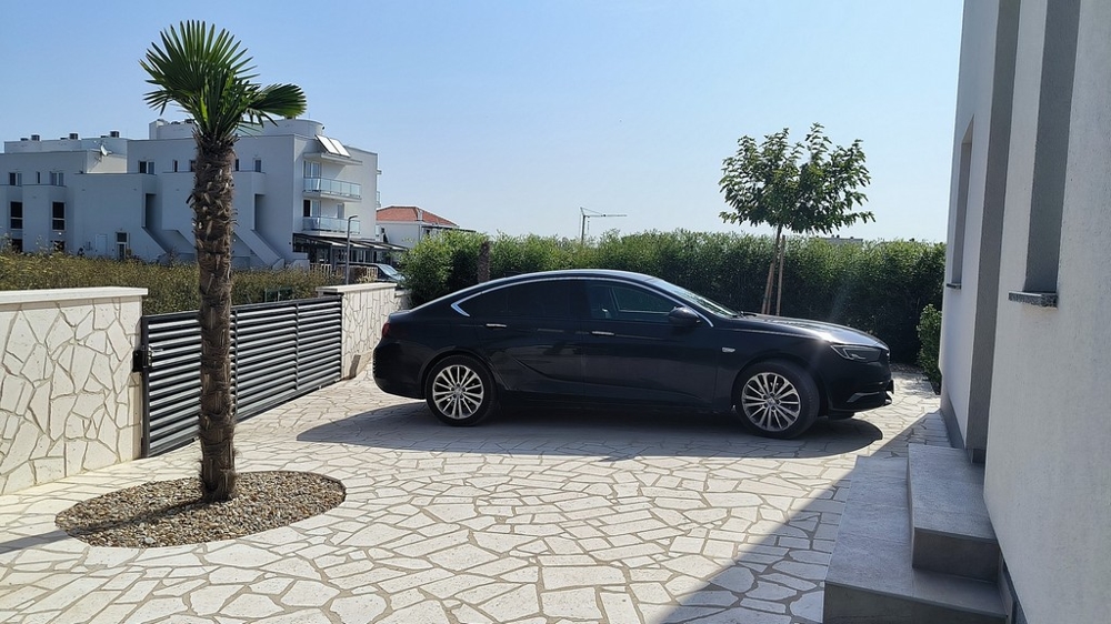 Wejście z samochodem, palmami i kamienną ścianą.