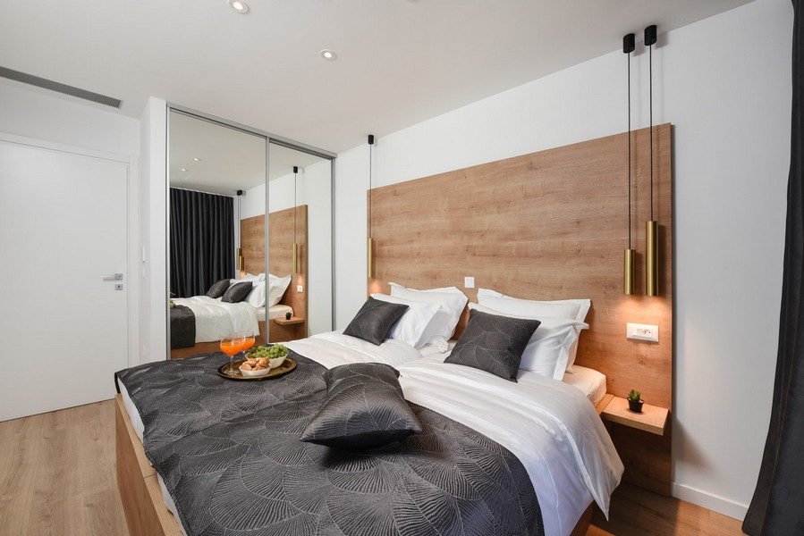 Nowocześnie urządzona sypialnia z drewnianymi elementami i lustrzaną szafą z przesuwanymi drzwiami.