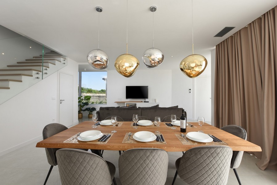Nowoczesna jadalnia z drewnianym stołem i designerskimi lampami w otwartej koncepcji życia.