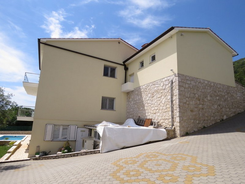 Wygląd zewnętrzny domu z utwardzonym parkingiem i basenem w tle.