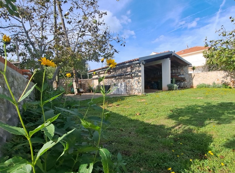 Teren zewnętrzny z trawnikiem, drzewami i kamienną konstrukcją.