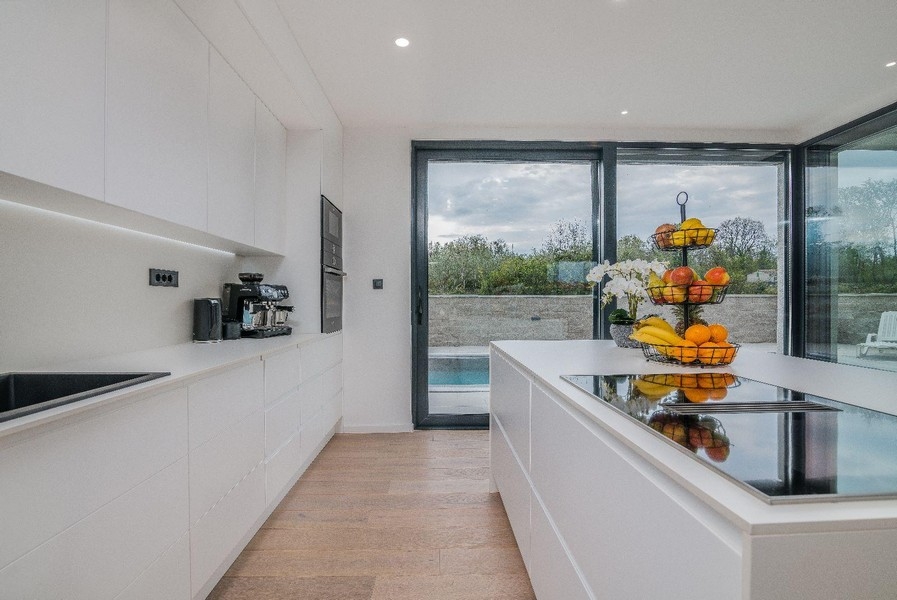 Nowoczesna biała kuchnia z widokiem na wyspę i basen