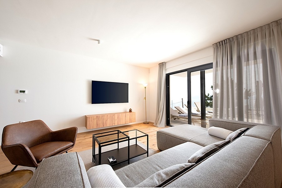 Pokój dzienny z szarą sofą, TV i wyjściem na taras