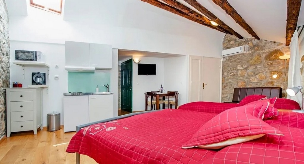 Studio z kamienną ścianą, podwójnym łóżkiem i aneksem kuchennym