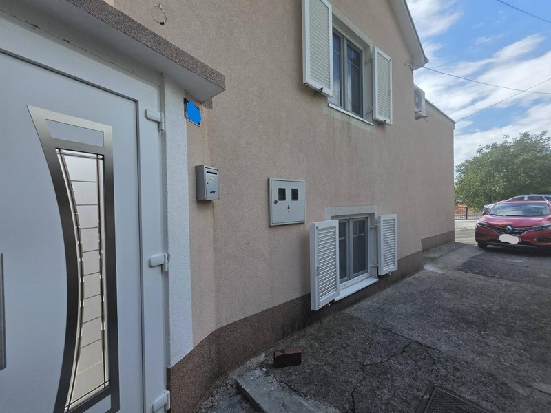 Fasada domu z drzwiami wejściowymi, okiennicami i miejscem parkingowym