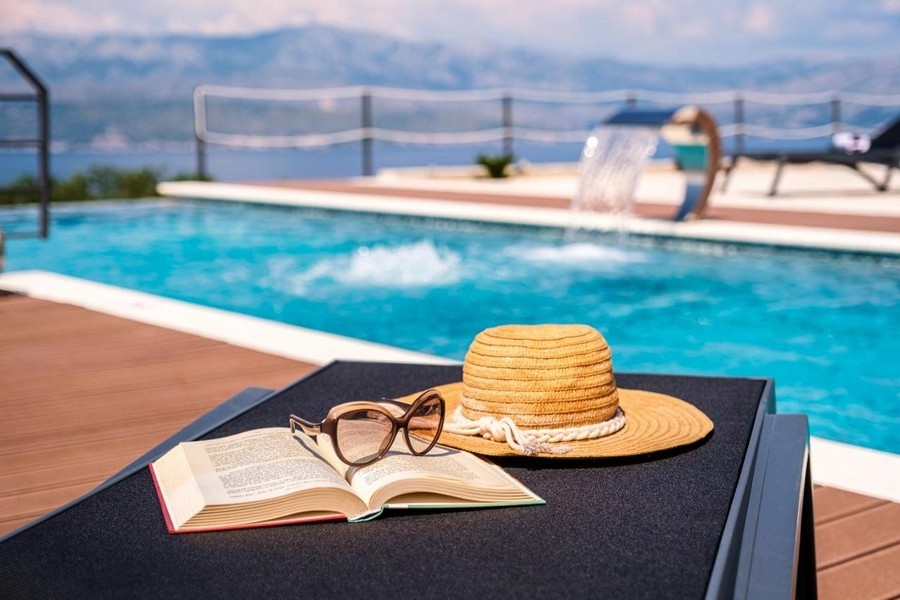 Szczegółowe ujęcie basenu z leżakiem, kapeluszem, okularami i książką