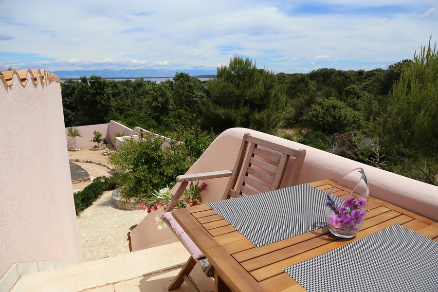 Taras z drewnianym stołem i krzesłami, widok na zieleń i morze