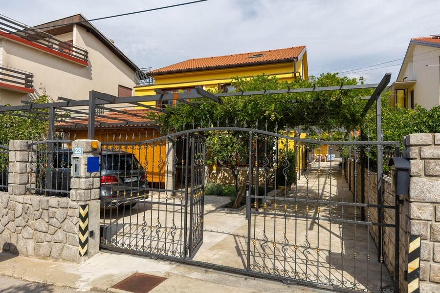 Wejście do nieruchomości z bramą i żółtym domem