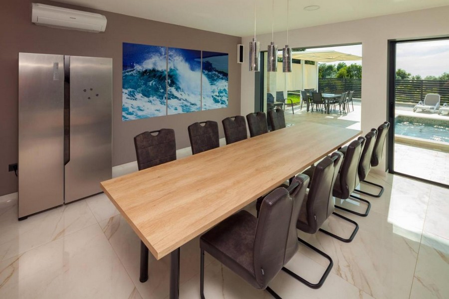 Jadalnia z dużym drewnianym stołem i dostępem do tarasu przy basenie