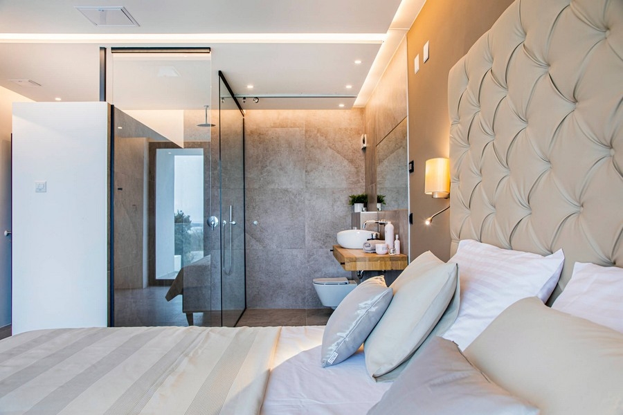 Sypialnia z przeszkloną łazienką i beżowym zagłówkiem.